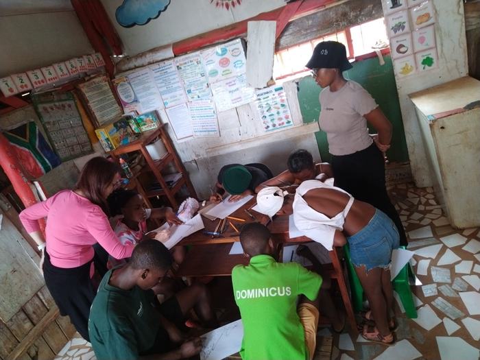 A facilitator helping young people with a drawing activity in a preschool classroom