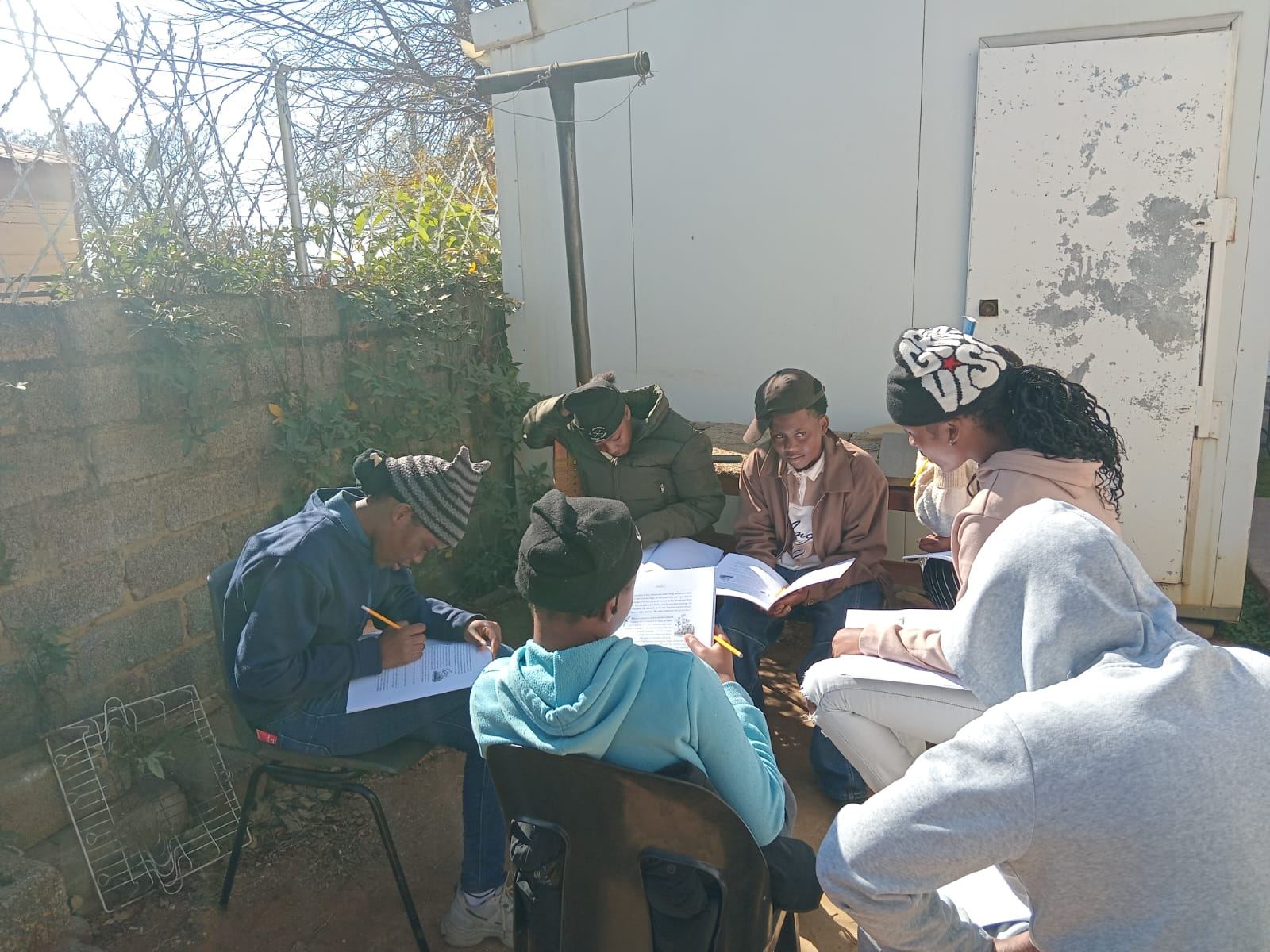 A junior youth group seated outdoors in winter coats, studying from a printed text together