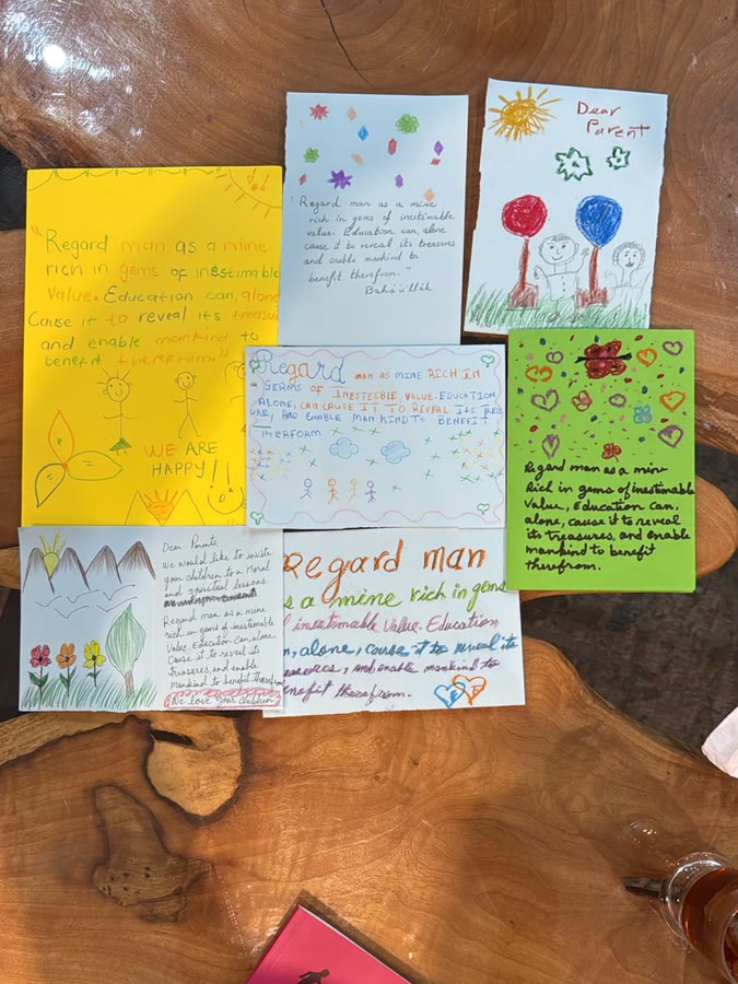 Seven hand-made cards laid out on a wooden table, each decorated with drawings and carrying the quotation 'Regard man as a mine rich in gems of inestimable value', some opening with 'Dear Parents'