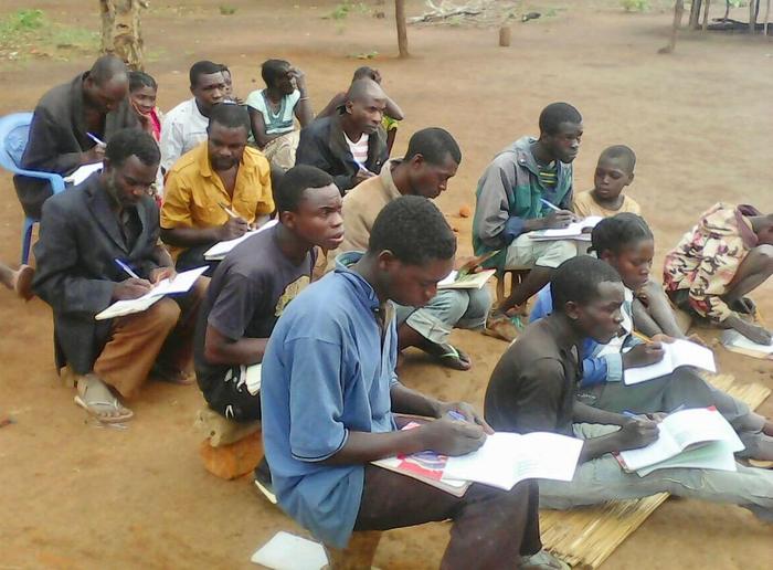 A study circle meeting outdoors, participants writing in exercise books