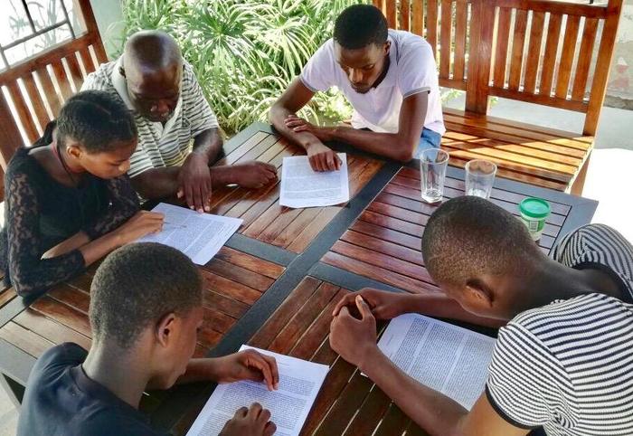 Five people studying printed material together around a table