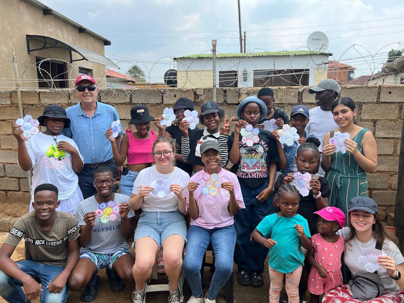 A large group of children, young people and adult volunteers together, each holding up a hexagonal piece of art they made in a Junior Youth session