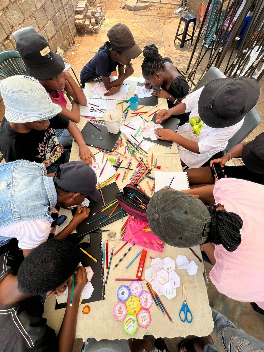 Junior youth colouring hexagonal artwork tiles around a table, pencils and papers spread across the surface